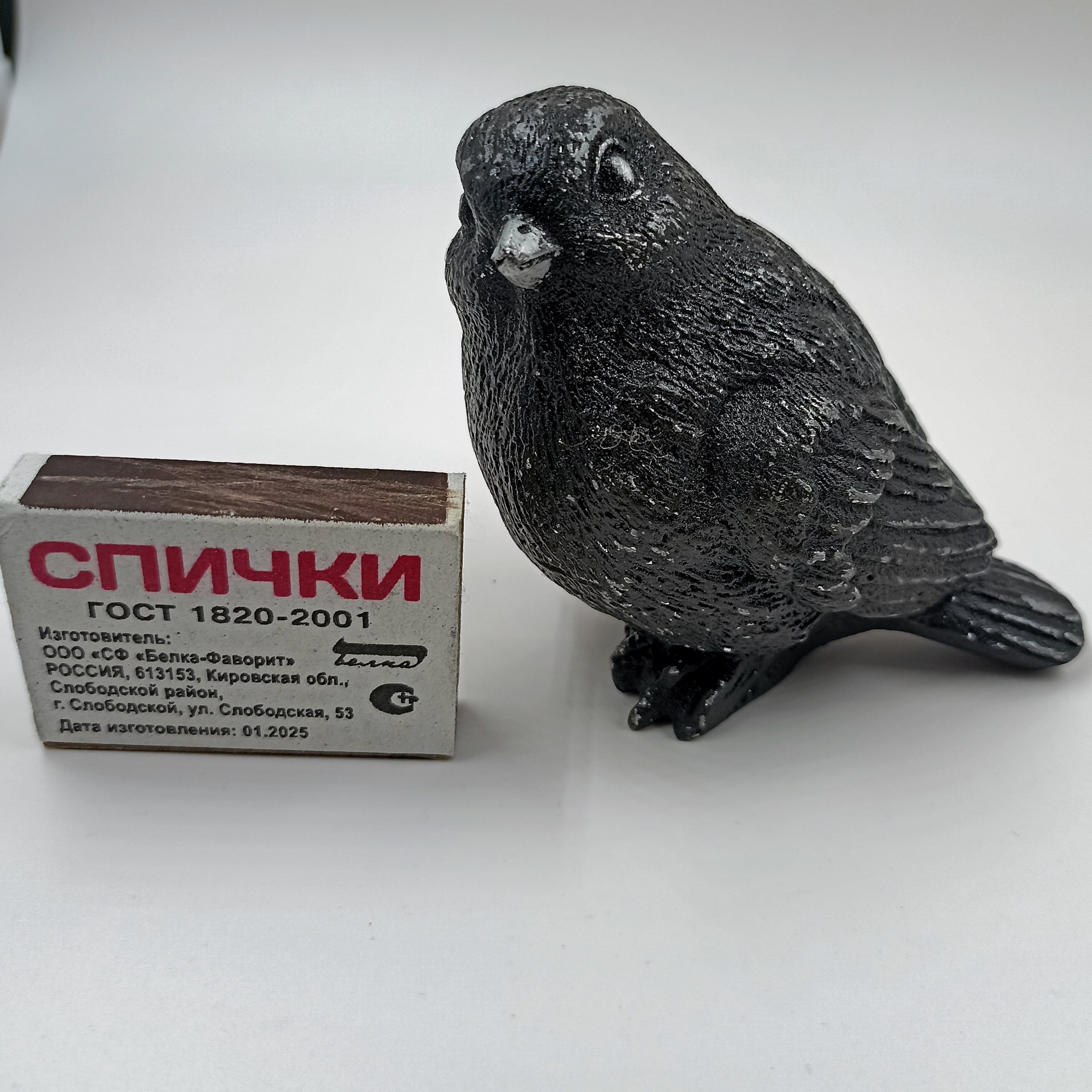 Литая птица-скворец рядом со спичечным коробком для масштаба